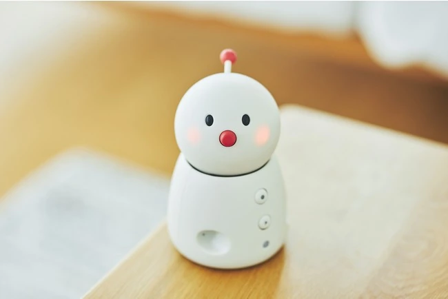BOCCO emo, a white tabletop robot with a red nose and red antenna, on a table.